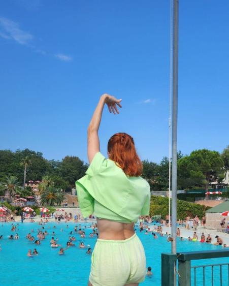 Frau in Grün tanzt vor einem vollen Pool.