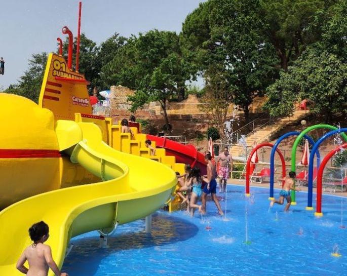 Children joyfully play among colorful slides and water sprays in a water park.